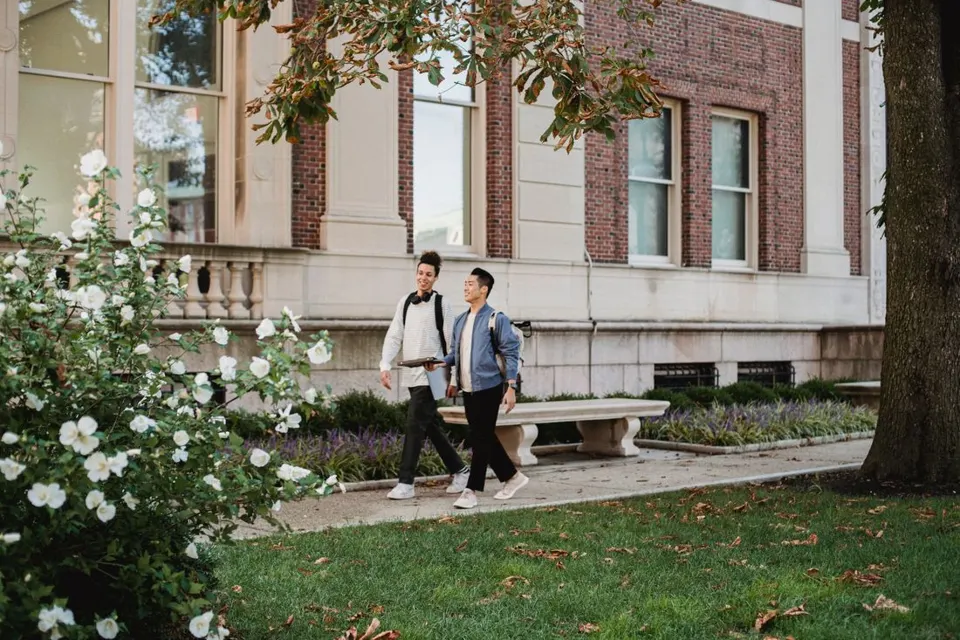 Two smiling students chatting as they walk along a campus path